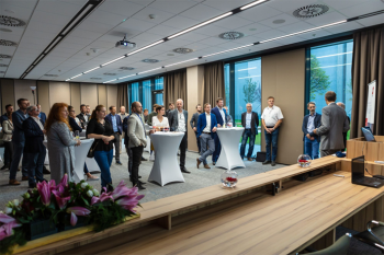 ľudia stojaci v konferenčnej miestnosti pri vysokých stolíkoch na otvorení novej kancelárie